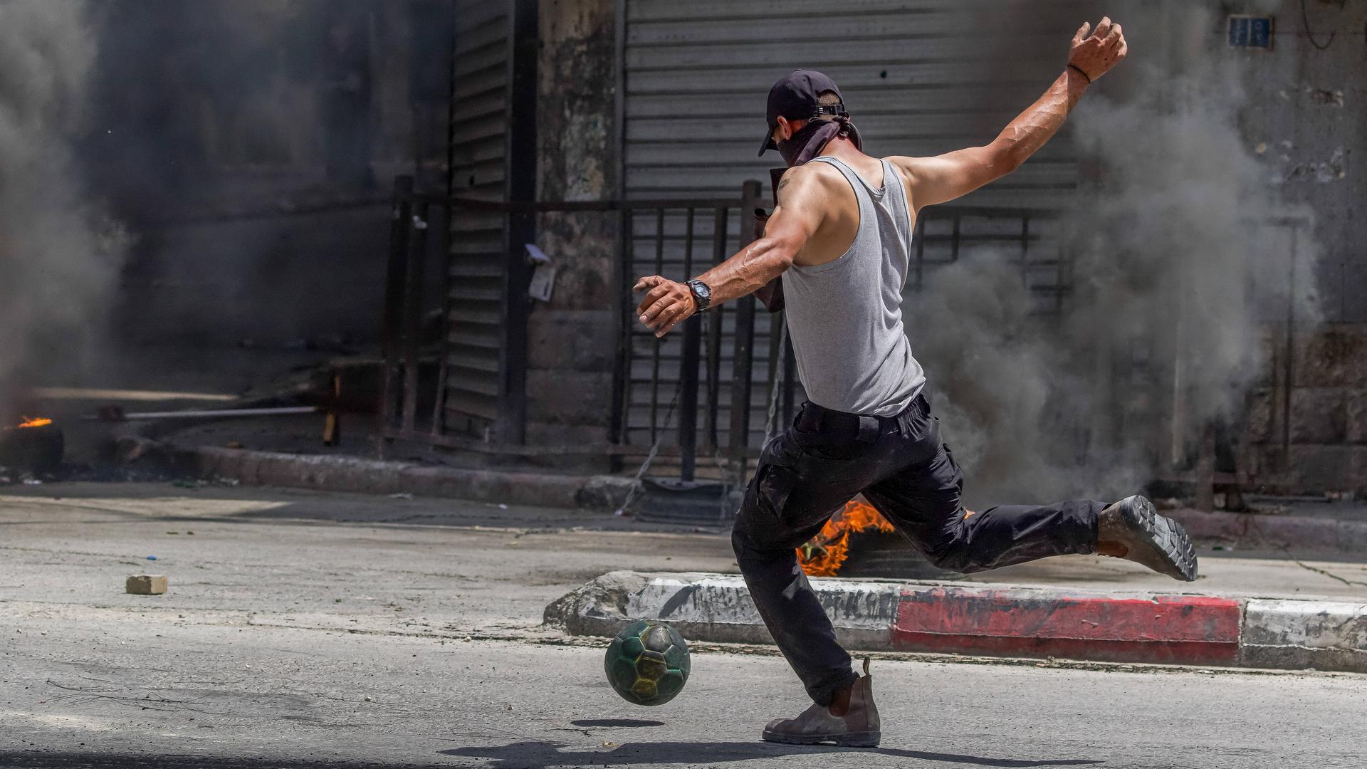 A Palestinian kicks a soccer ball away during unrest in the West Bank.