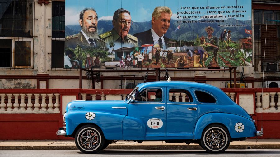 PhotoGalleria An old American car passes near a poster of the late Cuban leader Fidel Castro, former president Raúl Castro and current president Miguel Díaz-Canel in Havana