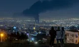 Smoke clouds hang above Tehran after an Israeli air raid on June 14, 2025. People watch a nearby hill.