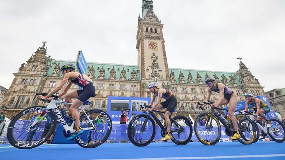 Participants of the triathlon drive past the Hamburg town hall.