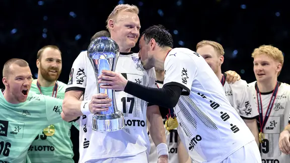 Kiels Patrick Wiencek holds the DHB Cup in his hands, Domagoj Duvnjak kisses his shoulder.