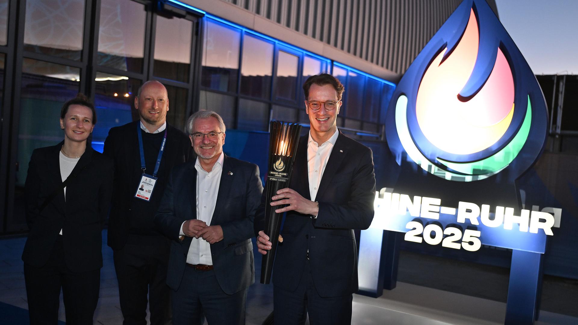 The Rhein-Ruhr organization team of World University Games 2025 around Managing Director Niklas Börger (2nd VL) poses with Hendrik Wüst, Prime Minister of NRW, with the torch in front of the event logo.