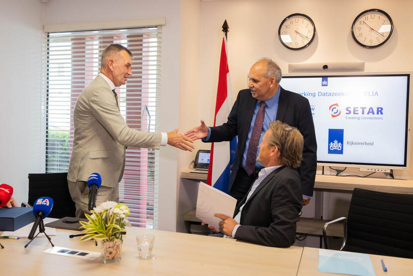 State Secretary Eddie van Marum (Left) gives Setar Director Roland Croes a hand during the press moment on Aruba, while SSCS Director Werner (sitting) Haan is watching.
