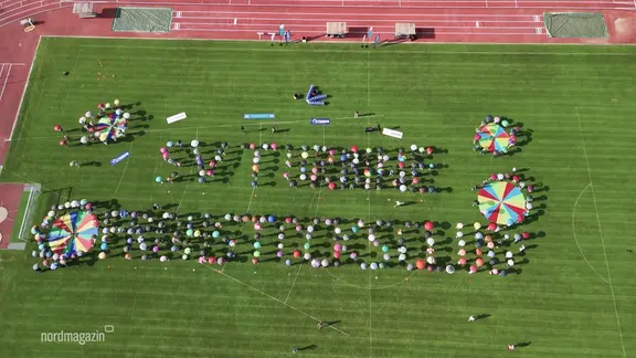 People stand on a sports field and form a lettering with umbrellas.