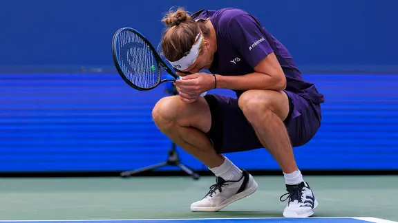 Tennis player Alexander Zverev crouches and has his face in his hands.