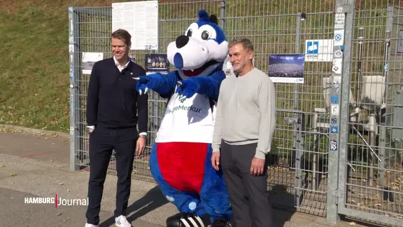 Two football managers stand next to the mascot of the HSV.