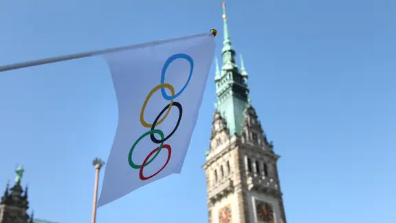 A flag with the Olympic rings hangs on a lamp post in front of Hamburg City Hall.