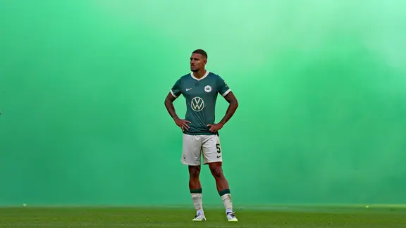 Vinicius Souza from VfL Wolfsburg stands in the green pyroscopic smoke