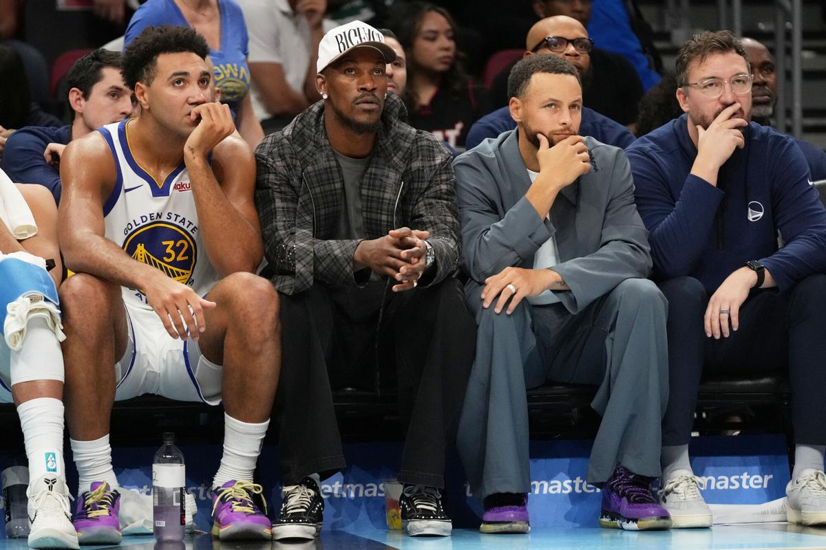 Golden State Warriors forward Trayce Jackson-Davis (32), forward Jimmy Butler III, center, and guard Stephen Curry, second from right, watch during the second half of an NBA basketball game against the Miami Heat, Wednesday, Nov. 19, 2025, in Miami. (AP Photo/Lynne Sladky)