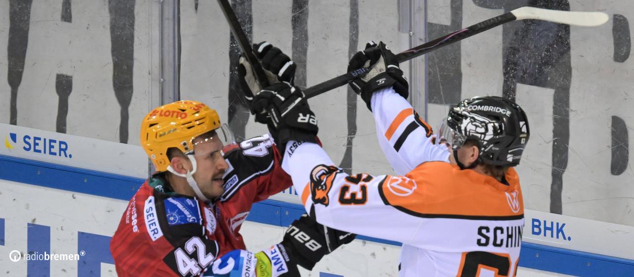 Two players from the Fischtown Pinguins and Grizzlys Wolfsburg attack each other with their ice hockey sticks.