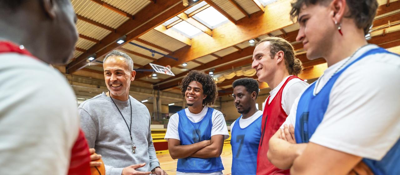 Basketball coach holds a clipboard and is surrounded by players