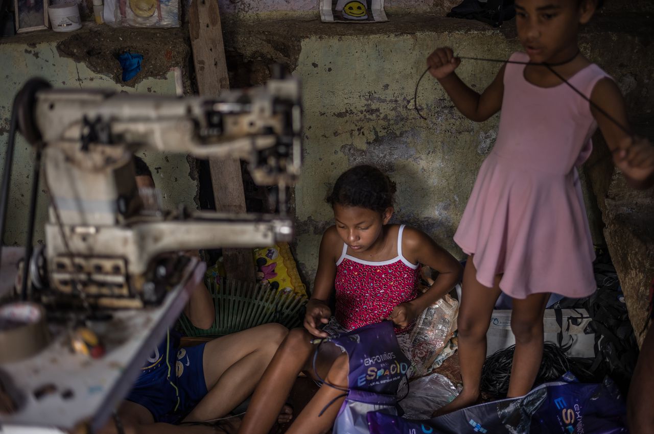 A child threads a shoelace through a plastic bag as part of her work.