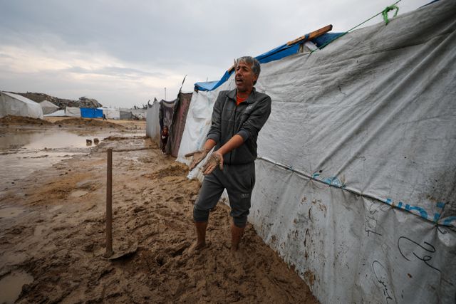 In Gaza City, a Palestinian man stands in the mud next to tents where displaced people sleep. 