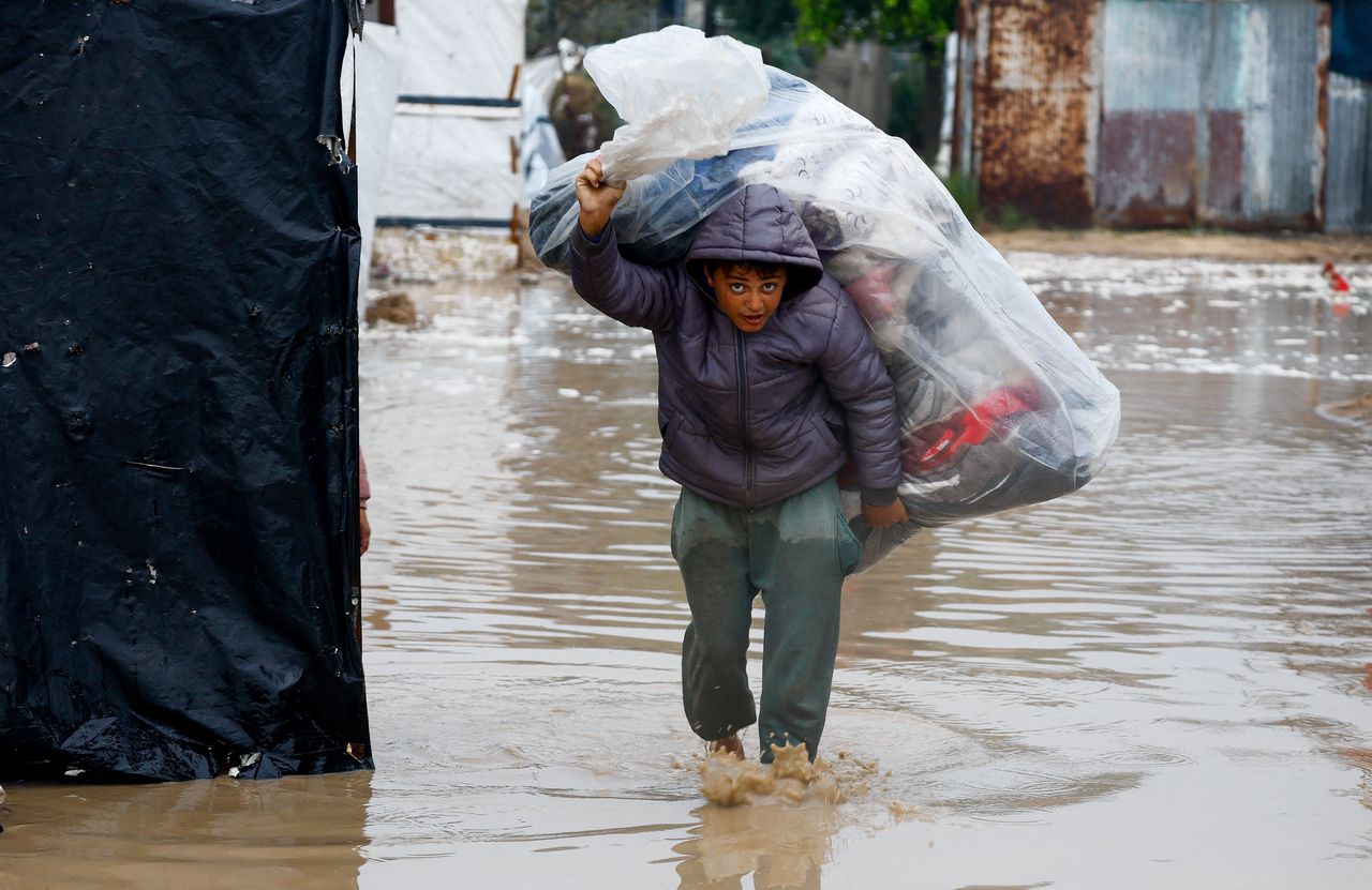 A displaced boy carries all his belongings in a large bag through the flooded streets of Nuseirat. 