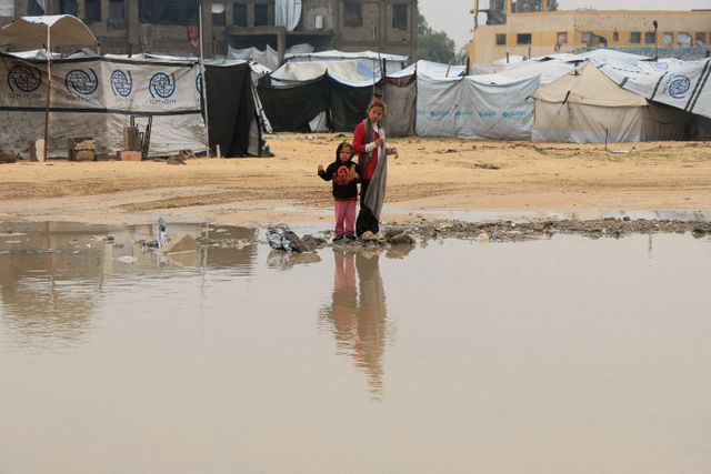 Displaced Palestinian children stand in a tent camp after a rainy day in Khan Younis. 