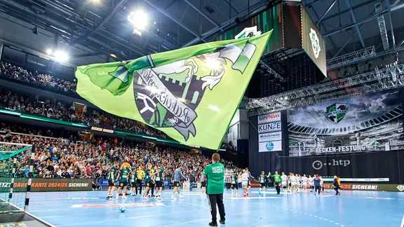 A man waves the flag of the handball Bundesliga team Hannover-Burgdorf in front of fans in the ZAG Arena.