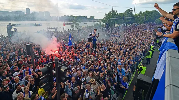 A bus with HSV players is accompanied by fans.