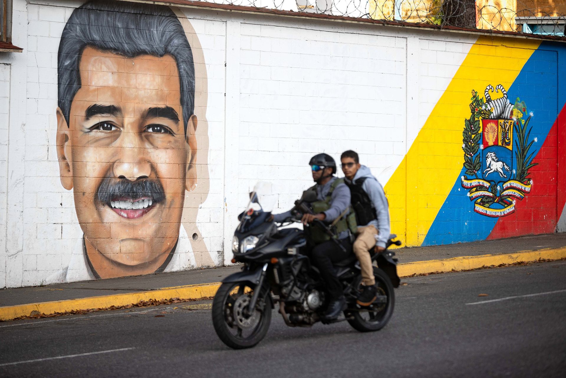 People ride on motorcycles past a mural of former Venezuelan President Nicolás Maduro on Sunday in Caracas.