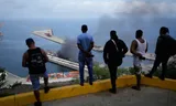 Men look out over the port of La Guaira, where clouds of smoke rise after a US attack. 
