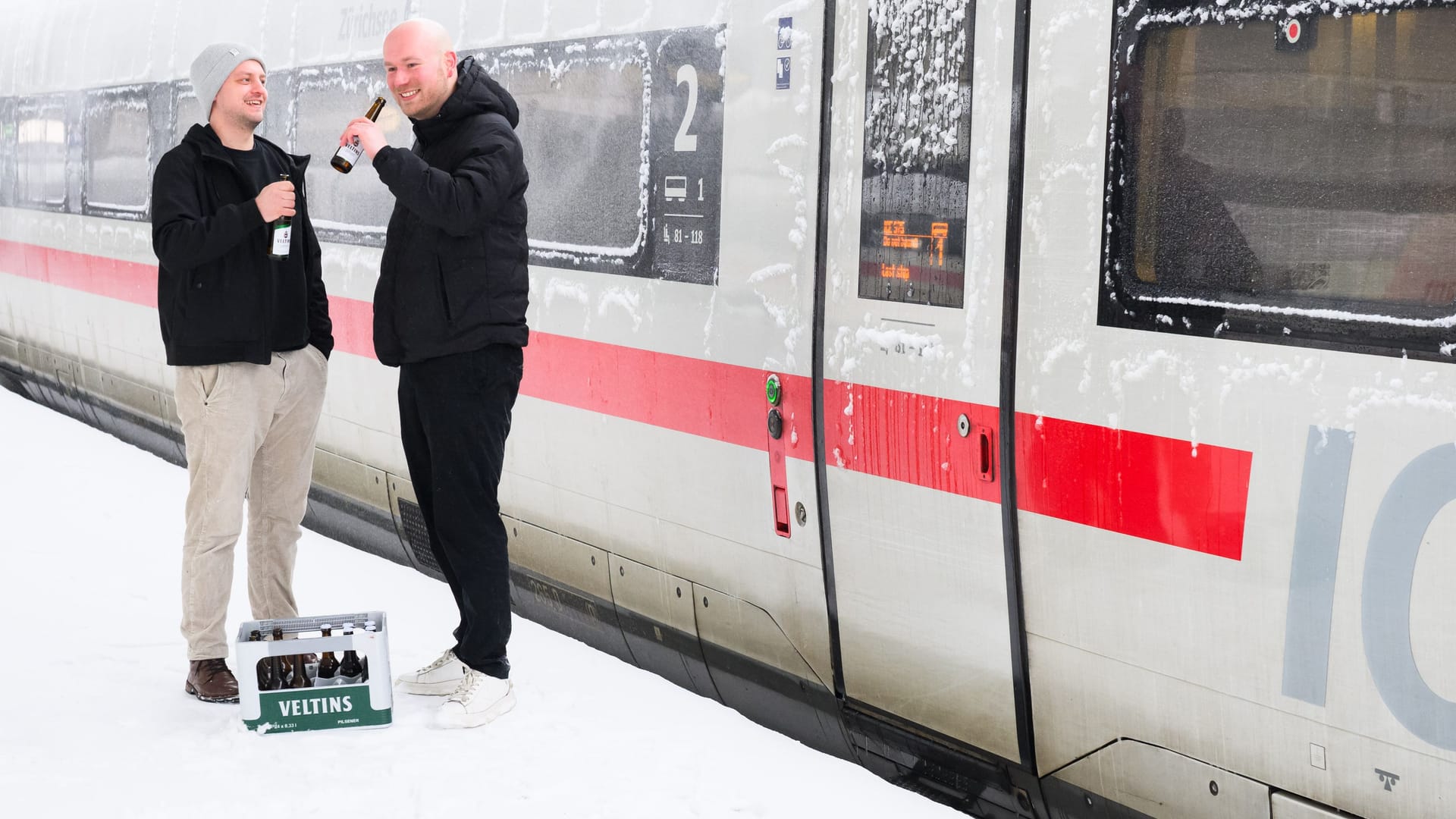 Two HSV fans stand with beer in front of a snow-covered train: Sturmtief "Elli" It makes traveling to the away game in Freiburg more difficult.
