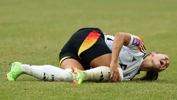 National player Lena Oberdorf lies on the grass and holds her knee. | IMAGO / Jan Huebner National player Lena Oberdorf lies on the grass and holds her knee.