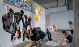 In the Nest exhibition space, in the Laak district of The Hague, volunteers are working on a giant tapestry that depicts the slavery past of South Holland, designed by Marcos Kueh. 
