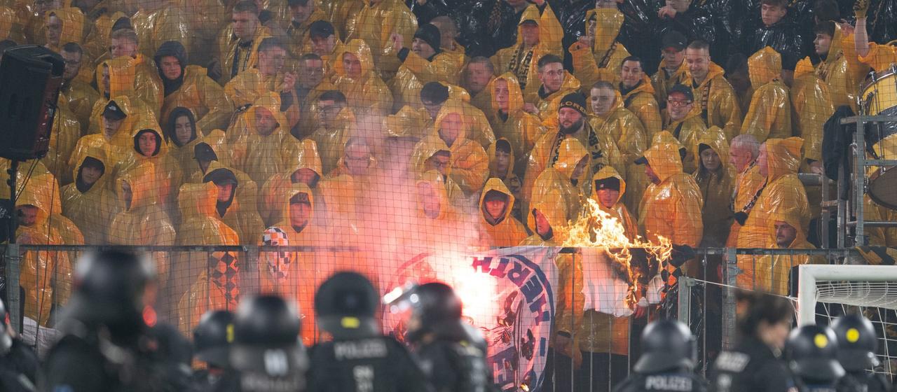 Police officers stand in front of the K-Block with Dresden fans during a break in the game in the stadium
