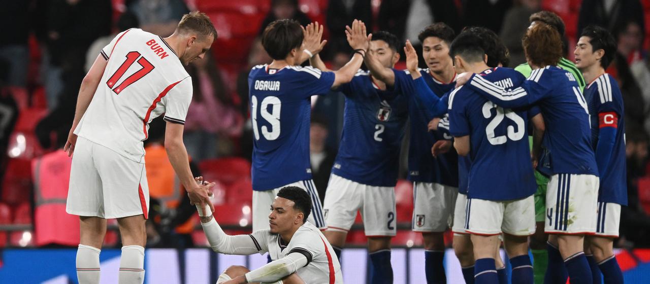 The Japanese celebrate winning the friendly against England - in the foreground sits the disappointed Morgan Rogers (2nd from left)