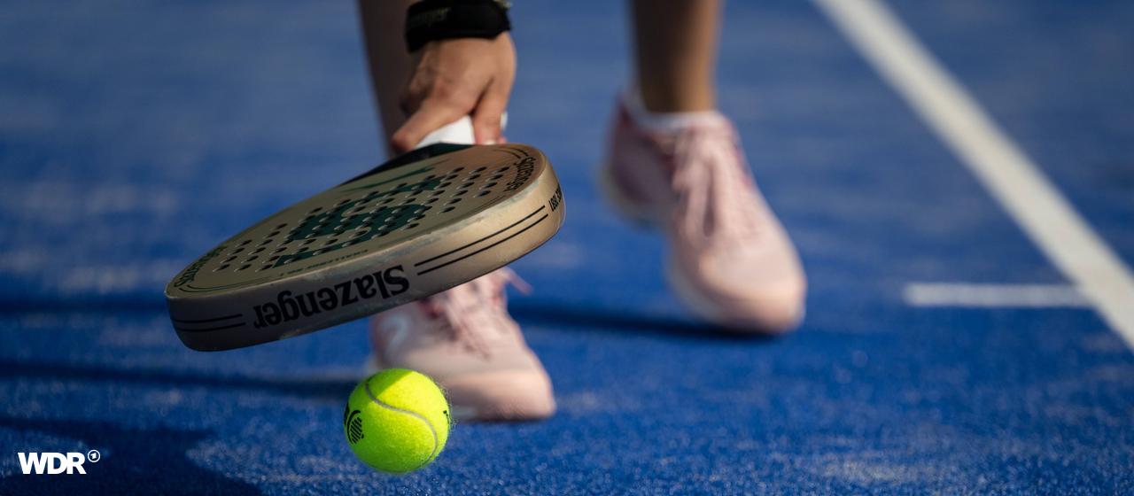 A padel player picks up a ball with his racket.