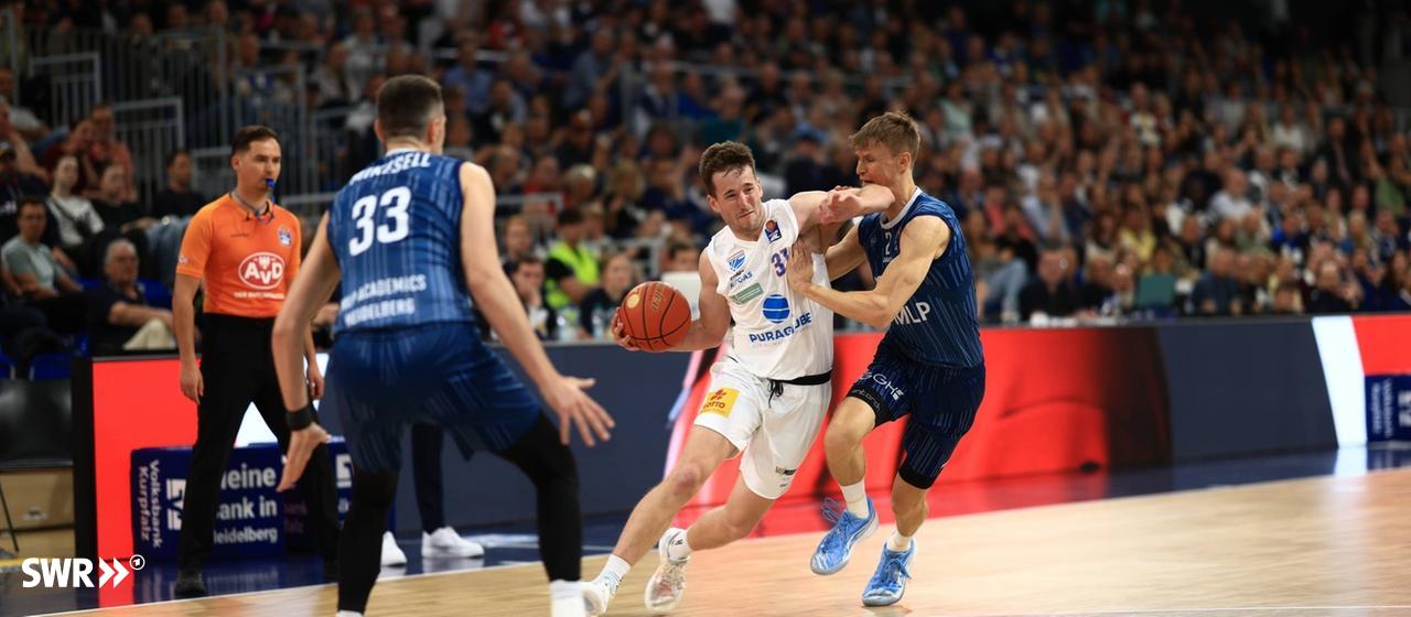 Michael Weathers (MLP Academics Heidelberg) dribbles energetically at the basket while Akeem Vargas (Syntainics MBC from Weiénfels) defends.