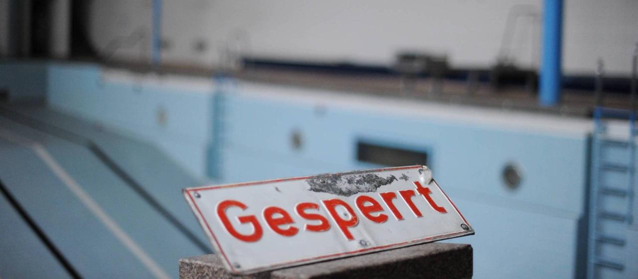 Sign with the inscription "Blocked" in front of an empty swimming pool