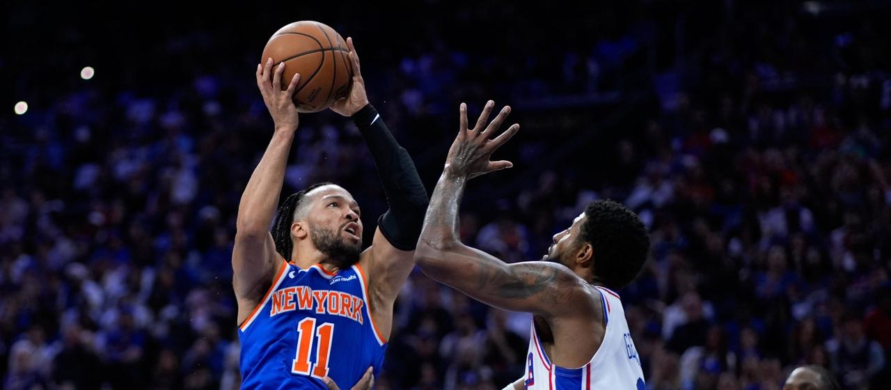 New York Knicks' Jalen Brunson (l.) prevails in the air against Philadelphia's Paul George