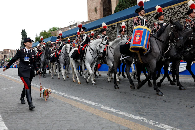 Carabinieri officers parade alongside an attendant walking a dog wearing a tricolor harness during the military parade.