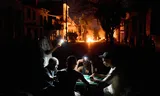 People illuminate themselves with their phones while playing dominoes as a fire set up by residents protesting against prolonged power outages burns on a street in Havana, Cuba, Thursday, May 14, 2026. (AP Photo/Ramon Espinosa)