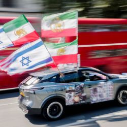 A car with American, Israeli and other flags from before the 1979 revolution flutters as it passes a group of anti-Iranian regime protesters gathered in front of Parliament in central London, England. | Photo:Brook Mitchell/AFP